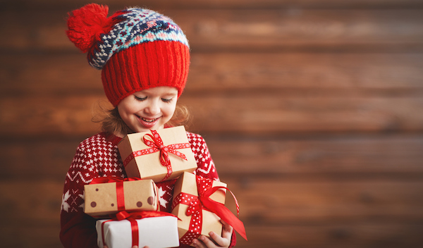 Little girl with red pom pom hat admiring her four red Christmas gifts featuring a wooden background