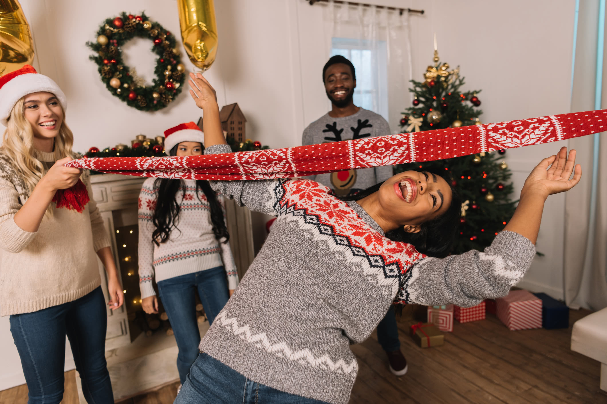 A group of friends playing limbo using a festive red scarf while celebrating christmas together