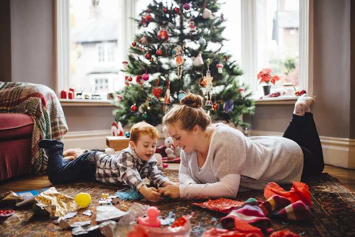 A young mother and her son celebrating Christmas morning together as they lie on the floor and playing with newly opened toys together.