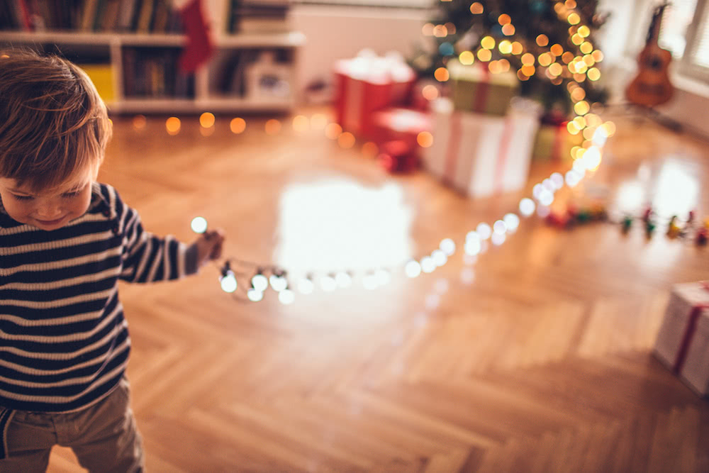 Little boy dragging along a string of bright christmas lights from a christmas tree