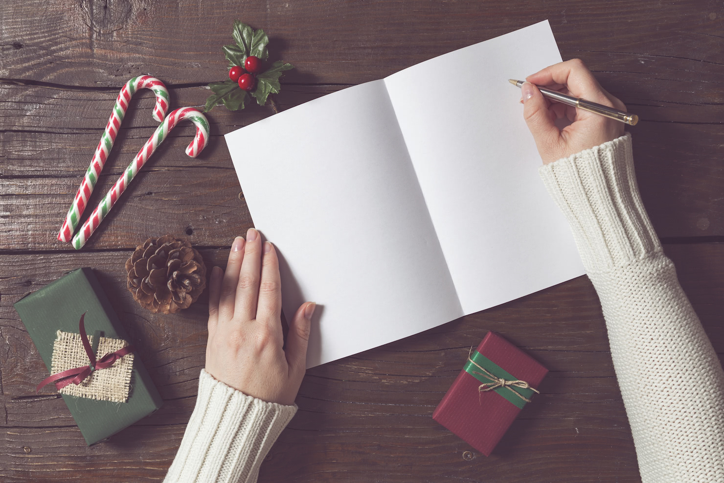 Woman preparing to write on a blank holiday business card featuring two gift packages candycanes and a pinecone