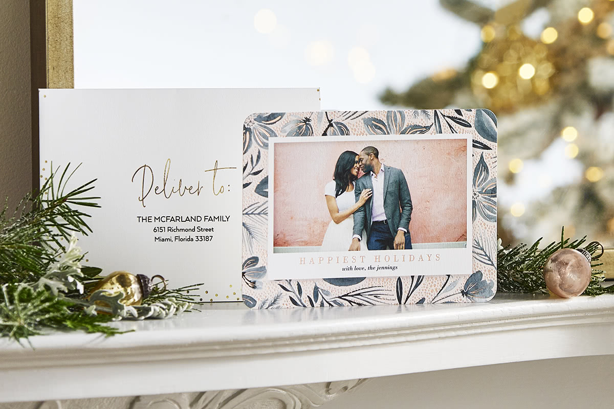 A custom envelope and personalized holiday card of a couple displayed on a white fireplace mantel 