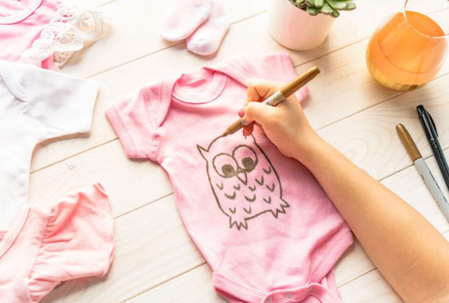 Woman drawing an owl with a gold marker on a pink onesie for an infant