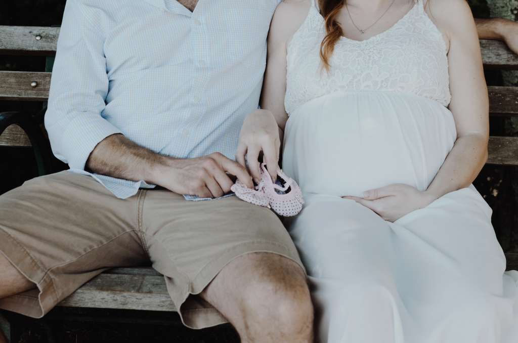 Couple making spring pregnancy announcement with baby shoes