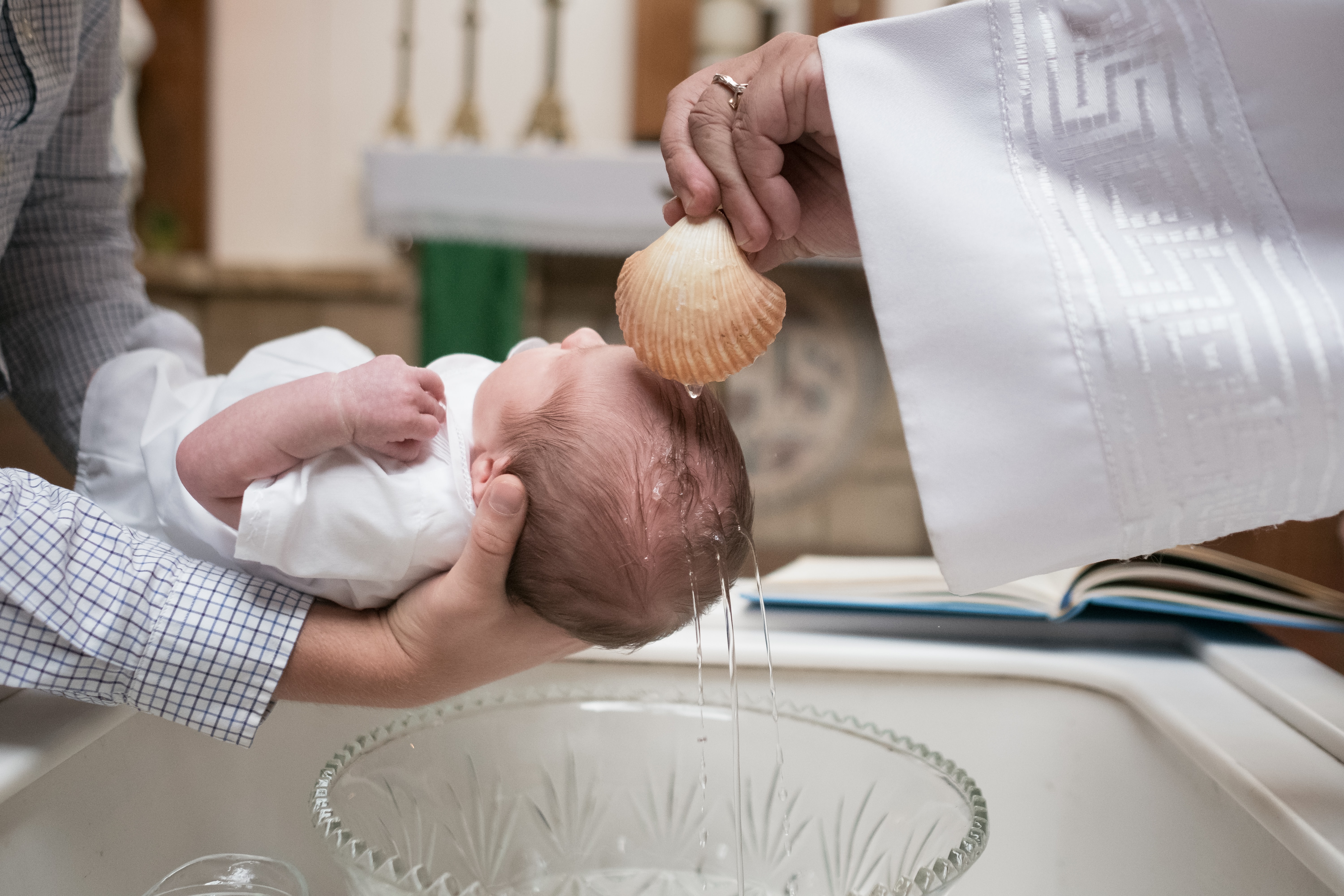 Father holding his baby while he is baptized from pastor in a church